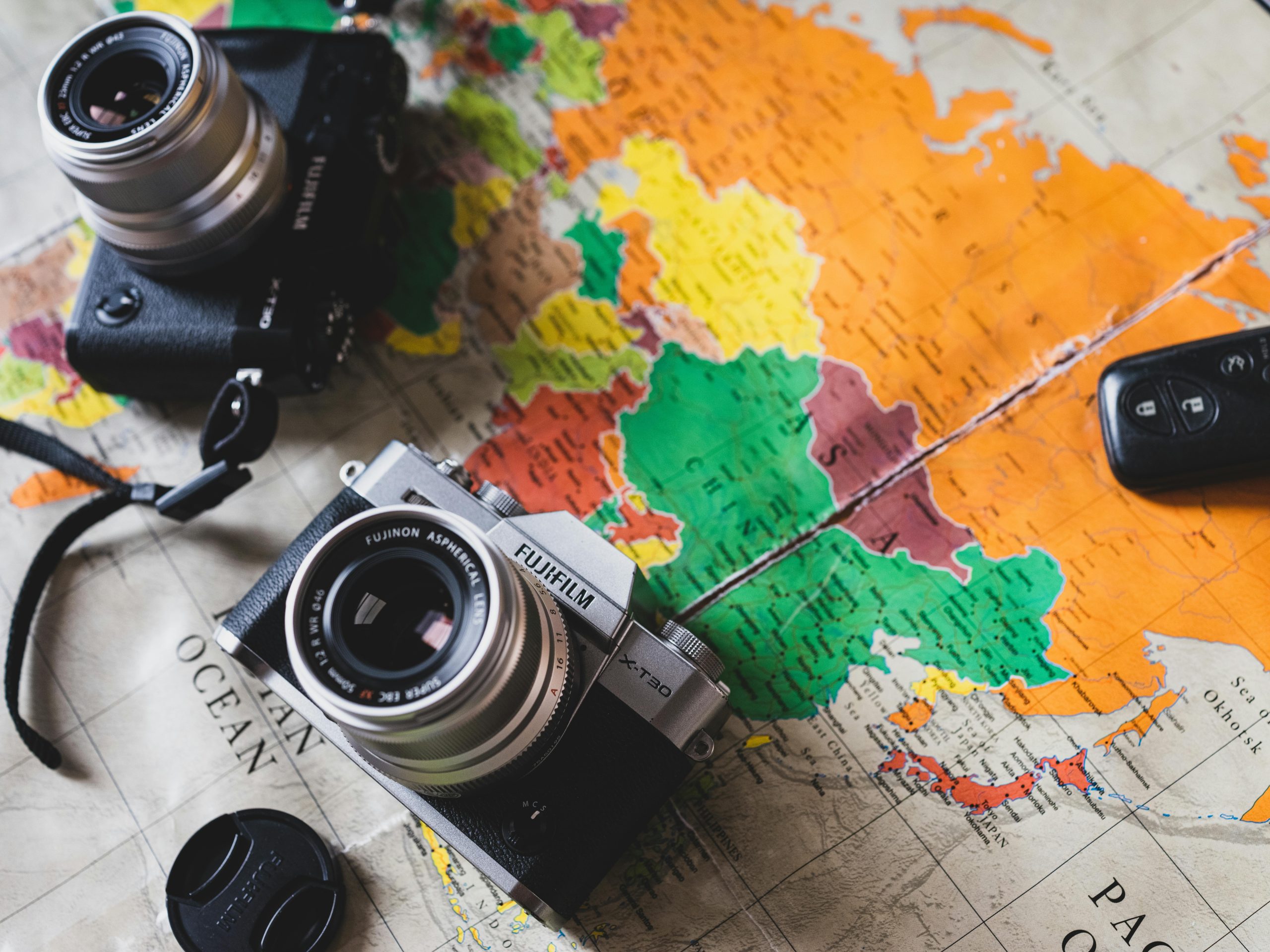 Two vintage cameras placed on a vibrant world map, showcasing travel themes.
